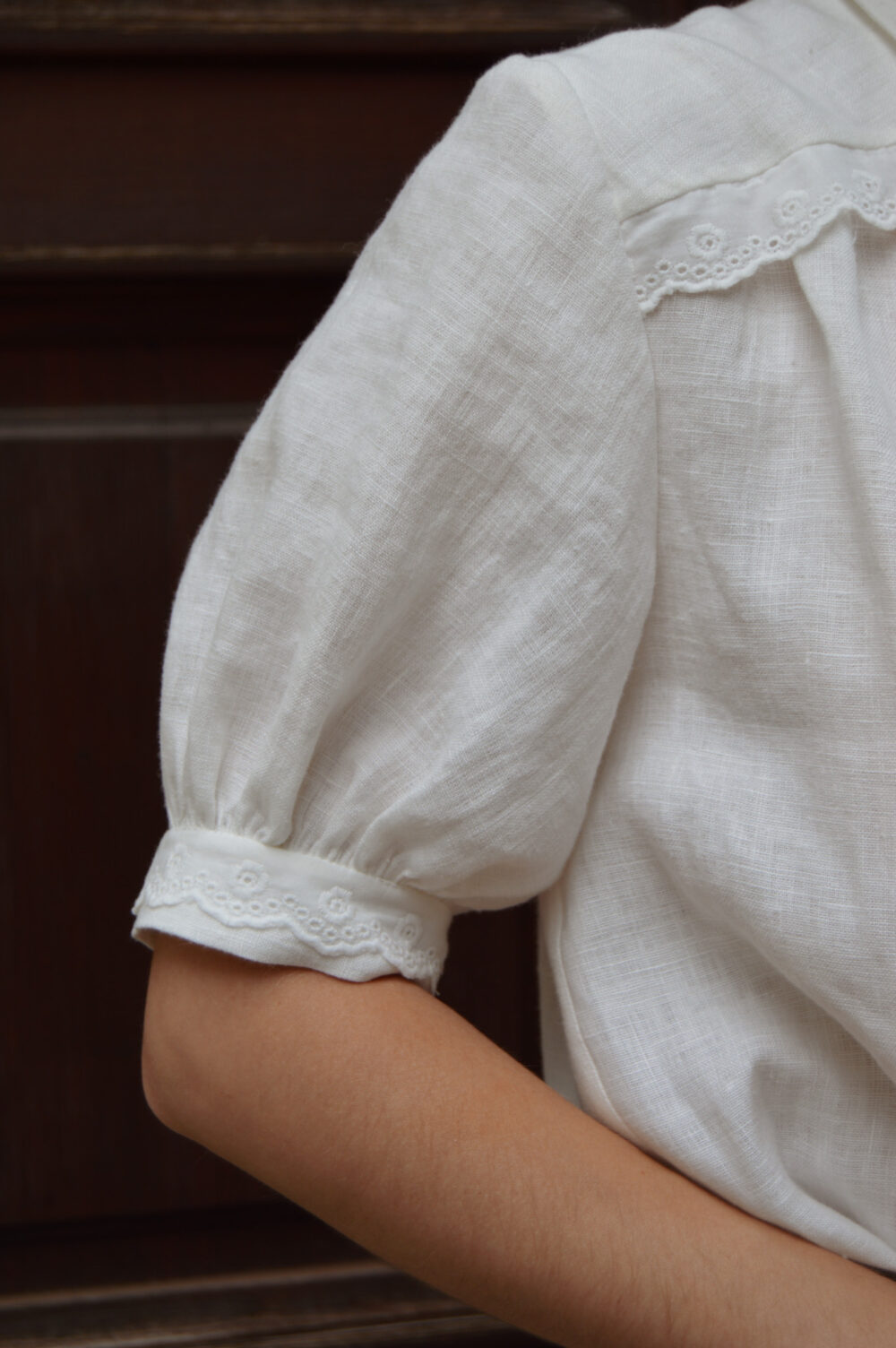 Lydia blouse sleeve slovakmeadows Woman wearing a light linen blouse with a V-neckline, collar, and lace details on the front, elbow-length sleeves.